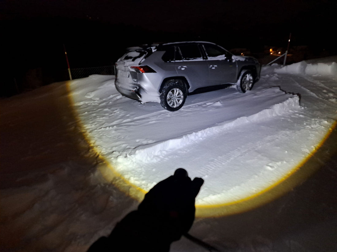 Persoon op besneeuwd bospad 's nachts verlicht door de krachtige straal van een felle LED zaklamp van aluminium.