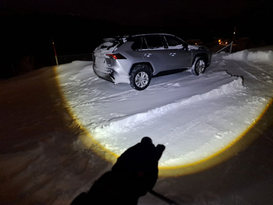 Persoon op besneeuwd bospad 's nachts verlicht door de krachtige straal van een felle LED zaklamp van aluminium.