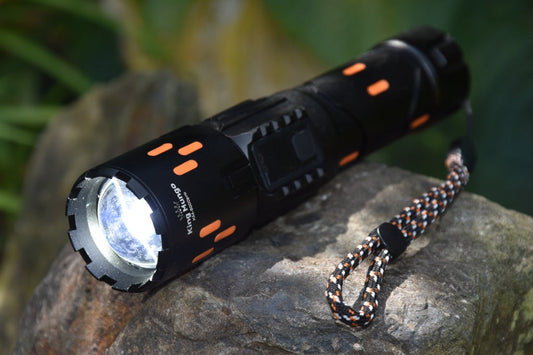Robuuste zwarte King Mungo 5000 pro LED zaklamp met oranje accenten rustend op een steen in de natuur.