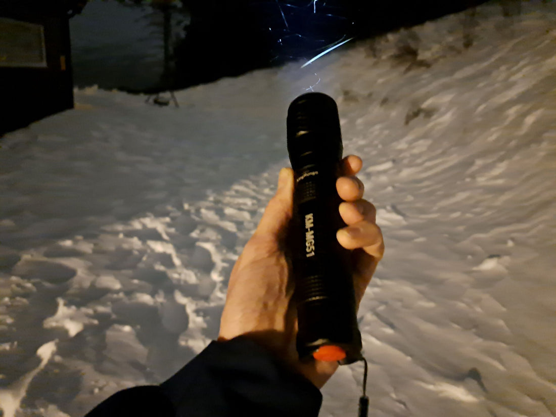 Hand die de zwarte King Mungo KM-MG51 aluminium zaklamp vasthoudt in de sneeuw tijdens een avondwandeling.